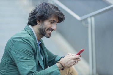 Arka planda bulanık bir manzara olan kapalı alanda akıllı telefon kullanan genç bir adamın görüntüsü. Yüksek kalite fotoğraf. Telefondaki mesajlaşma.. 