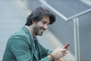 Arka planda bulanık bir manzara olan kapalı alanda akıllı telefon kullanan genç bir adamın görüntüsü. Yüksek kalite fotoğraf. Telefondaki mesajlaşma.. 