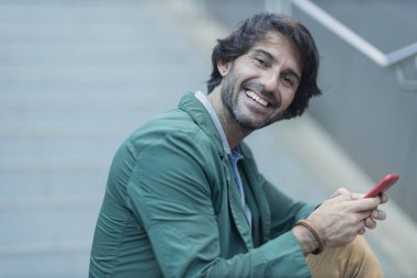 Arka planda bulanık bir manzara olan kapalı alanda akıllı telefon kullanan genç bir adamın görüntüsü. Yüksek kalite fotoğraf. Telefondaki mesajlaşma.. 