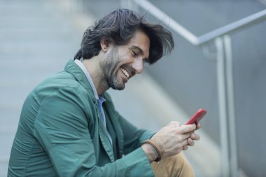 Arka planda bulanık bir manzara olan kapalı alanda akıllı telefon kullanan genç bir adamın görüntüsü. Yüksek kalite fotoğraf. Telefondaki mesajlaşma.. 