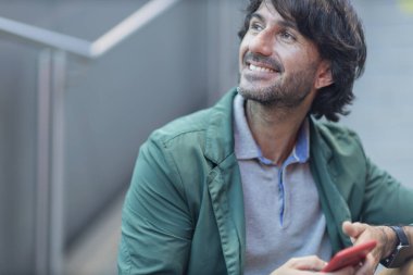 Arka planda bulanık bir manzara olan kapalı alanda akıllı telefon kullanan genç bir adamın görüntüsü. Yüksek kalite fotoğraf. Telefondaki mesajlaşma.. 