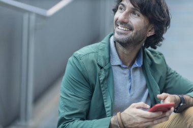 Arka planda bulanık bir manzara olan kapalı alanda akıllı telefon kullanan genç bir adamın görüntüsü. Yüksek kalite fotoğraf. Telefondaki mesajlaşma.. 