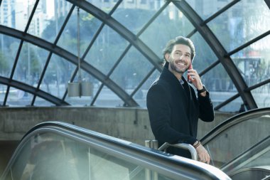 Arka planda bulanık bir manzara olan kapalı alanda akıllı telefon kullanan genç bir adamın görüntüsü. Yüksek kalite fotoğraf. Telefonda konuşuyorlar.. 