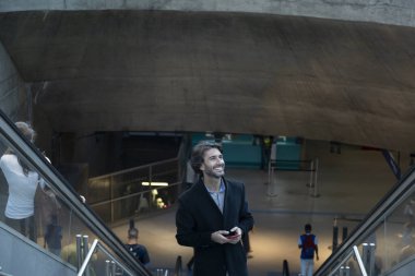 Arka planda bulanık bir manzara olan kapalı alanda akıllı telefon kullanan genç bir adamın görüntüsü. Yüksek kalite fotoğraf. Telefondaki mesajlaşma.. 