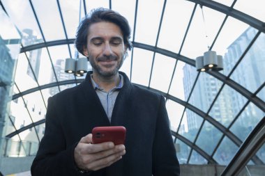 Arka planda bulanık bir manzara olan kapalı alanda akıllı telefon kullanan genç bir adamın görüntüsü. Yüksek kalite fotoğraf. Telefondaki mesajlaşma.. 