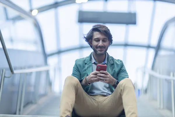Arka planda bulanık bir manzara olan kapalı alanda akıllı telefon kullanan genç bir adamın görüntüsü. Yüksek kalite fotoğraf. Telefondaki mesajlaşma.. 