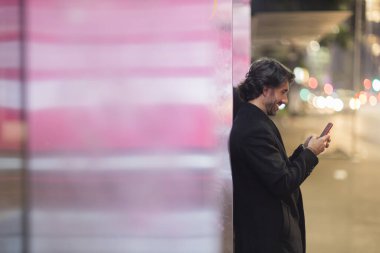 Gece vakti arka planda şehir manzarası olan akıllı telefon kullanan genç bir adamın görüntüsü. Yüksek kalite fotoğraf. Gece vakti arka planda şehir manzarası olan akıllı telefon kullanan genç bir adamın görüntüsü. Yüksek kalite fotoğraf. 