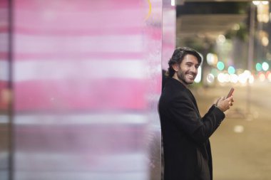 Gece vakti arka planda şehir manzarası olan akıllı telefon kullanan genç bir adamın görüntüsü. Yüksek kalite fotoğraf. Gece vakti arka planda şehir manzarası olan akıllı telefon kullanan genç bir adamın görüntüsü. Yüksek kalite fotoğraf. 