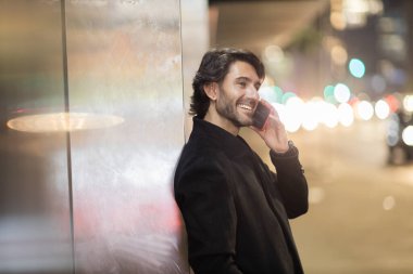 Gece vakti arka planda şehir manzarası olan akıllı telefon kullanan genç bir adamın görüntüsü. Yüksek kalite fotoğraf. Gece vakti arka planda şehir manzarası olan akıllı telefon kullanan genç bir adamın görüntüsü. Yüksek kalite fotoğraf.