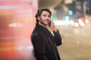 Gece vakti arka planda şehir manzarası olan akıllı telefon kullanan genç bir adamın görüntüsü. Yüksek kalite fotoğraf. Gece vakti arka planda şehir manzarası olan akıllı telefon kullanan genç bir adamın görüntüsü. Yüksek kalite fotoğraf.