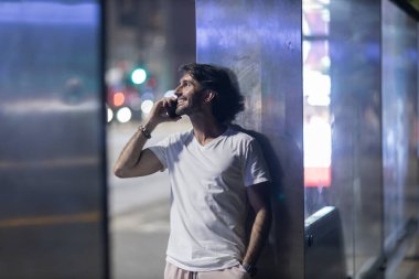 Gece vakti arka planda şehir manzarası olan akıllı telefon kullanan genç bir adamın görüntüsü. Yüksek kalite fotoğraf. Gece vakti arka planda şehir manzarası olan akıllı telefon kullanan genç bir adamın görüntüsü. Yüksek kalite fotoğraf.