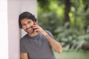 Şehirdeki yeşil bir parkta gündüz vakti akıllı telefonlu genç bir adam görülüyor..