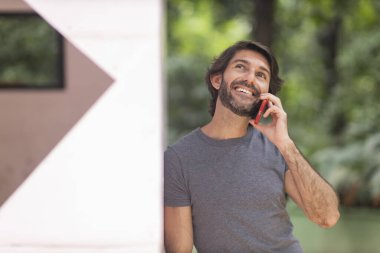 Şehirdeki yeşil bir parkta gündüz vakti akıllı telefonlu genç bir adam görülüyor..