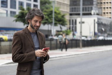 Gündüz vakti akıllı telefonlu genç bir adamın arka planda şehir manzaralı görüntüsü. Yüksek kalite fotoğraf.