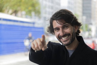 Arka planda şehir manzarası olan ve gündüz vakti kamerayı gösteren genç bir adamın görüntüsü. Yüksek kalite fotoğraf.