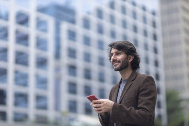 Gündüz vakti akıllı telefonlu genç bir adamın arka planda şehir manzaralı görüntüsü. Yüksek kalite fotoğraf.
