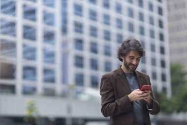 Gündüz vakti akıllı telefonlu genç bir adamın arka planda şehir manzaralı görüntüsü. Yüksek kalite fotoğraf.