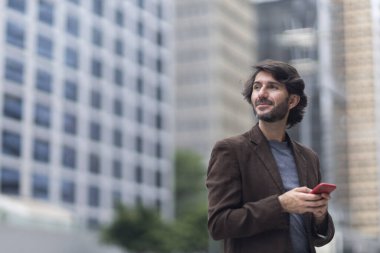 Gündüz vakti akıllı telefonlu genç bir adamın arka planda şehir manzaralı görüntüsü. Yüksek kalite fotoğraf.