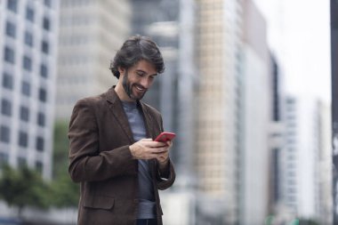 Gündüz vakti akıllı telefonlu genç bir adamın arka planda şehir manzaralı görüntüsü. Yüksek kalite fotoğraf.