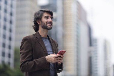 Gündüz vakti akıllı telefonlu genç bir adamın arka planda şehir manzaralı görüntüsü. Yüksek kalite fotoğraf.