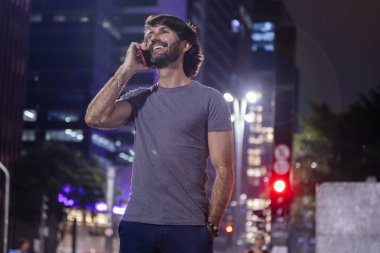 Gece vakti akıllı telefon kullanan genç bir adam. Şehir manzarası ve arka planda araba trafiği var.. 