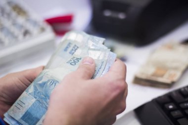 Değişim bürosu / bankada çalışan iş adamının insan eli. O para sayıyor ve bir müşteriye nakit para veriyor. Brezilya Reais 100 reais.