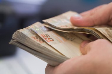 Değişim bürosu / bankada çalışan iş adamının insan eli. O para sayıyor ve bir müşteriye nakit para veriyor. Brezilyalı 50 reais fatura.