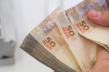 Değişim bürosu / bankada çalışan iş adamının insan eli. O para sayıyor ve bir müşteriye nakit para veriyor. Brezilyalı 50 reais fatura.