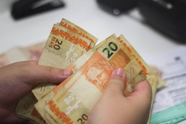 Değişim bürosu / bankada çalışan iş adamının insan eli. O para sayıyor ve bir müşteriye nakit para veriyor. Brezilyalı 50 reais fatura.