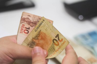 Değişim bürosu / bankada çalışan iş adamının insan eli. O para sayıyor ve bir müşteriye nakit para veriyor. Brezilyalı Reais.
