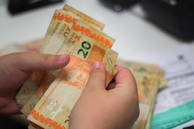 Değişim bürosu / bankada çalışan iş adamının insan eli. O para sayıyor ve bir müşteriye nakit para veriyor. Brezilya Reais - 20 reais fatura.