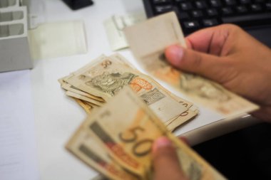 Değişim bürosu / bankada çalışan iş adamının insan eli. O para sayıyor ve bir müşteriye nakit para veriyor. Brezilyalı 50 reais fatura.