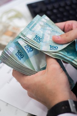 Değişim bürosu / bankada çalışan iş adamının insan eli. O para sayıyor ve bir müşteriye nakit para veriyor. Brezilya Reais 100 reais.
