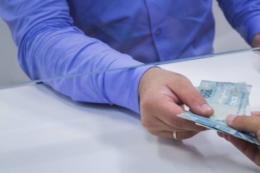 Değişim bürosu / bankada çalışan iş adamının insan eli. O para sayıyor ve bir müşteriye nakit para veriyor. Brezilya Reais 100 reais.