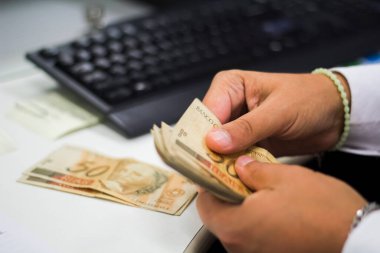 Değişim bürosu / bankada çalışan iş adamının insan eli. O para sayıyor ve bir müşteriye nakit para veriyor. Brezilyalı 50 reais fatura.