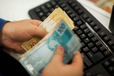 Değişim bürosu / bankada çalışan iş adamının insan eli. O para sayıyor ve bir müşteriye nakit para veriyor. Brezilyalı Reais.