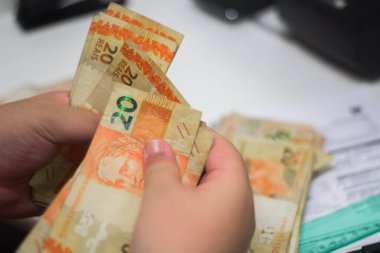 Değişim bürosu / bankada çalışan iş adamının insan eli. O para sayıyor ve bir müşteriye nakit para veriyor. Brezilya Reais - 20 reais fatura.