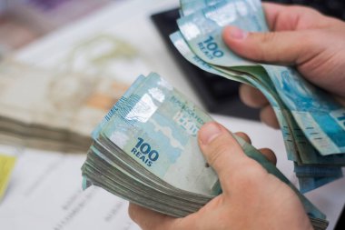 Değişim bürosu / bankada çalışan iş adamının insan eli. O para sayıyor ve bir müşteriye nakit para veriyor. Brezilya Reais 100 reais.
