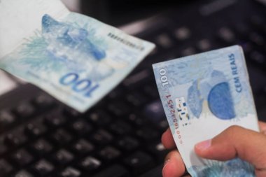 Değişim bürosu / bankada çalışan iş adamının insan eli. O para sayıyor ve bir müşteriye nakit para veriyor. Brezilya Reais 100 reais.