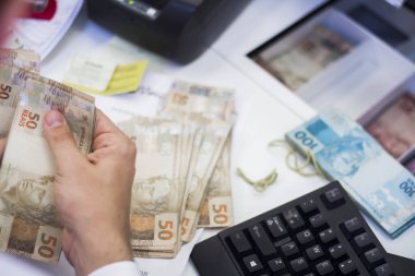 Değişim bürosu / bankada çalışan iş adamının insan eli. O para sayıyor ve bir müşteriye nakit para veriyor. Brezilyalı Reais.