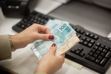 Değişim bürosu / bankada çalışan iş adamının insan eli. O para sayıyor ve bir müşteriye nakit para veriyor. Brezilyalı Reais.