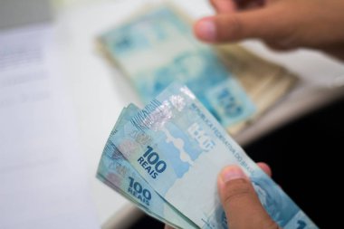Değişim bürosu / bankada çalışan iş adamının insan eli. O para sayıyor ve bir müşteriye nakit para veriyor. Brezilya Reais 100 reais.