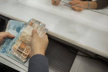 Değişim bürosu / bankada çalışan iş adamının insan eli. O para sayıyor ve bir müşteriye nakit para veriyor. Brezilyalı Reais.