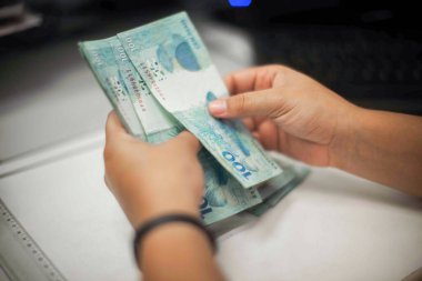 Değişim bürosu / bankada çalışan iş adamının insan eli. O para sayıyor ve bir müşteriye nakit para veriyor. Brezilya Reais 100 reais.