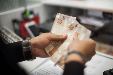 Değişim bürosu / bankada çalışan iş adamının insan eli. O para sayıyor ve bir müşteriye nakit para veriyor. Brezilyalı 50 reais fatura.