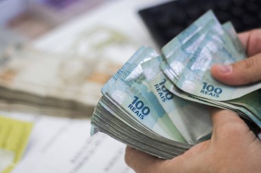 Değişim bürosu / bankada çalışan iş adamının insan eli. O para sayıyor ve bir müşteriye nakit para veriyor. Brezilya Reais 100 reais.