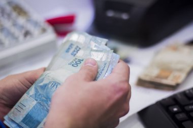 Değişim bürosu / bankada çalışan iş adamının insan eli. O para sayıyor ve bir müşteriye nakit para veriyor. Brezilya Reais 100 reais.