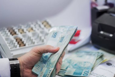Değişim bürosu / bankada çalışan iş adamının insan eli. O para sayıyor ve bir müşteriye nakit para veriyor. Brezilya Reais 100 reais.