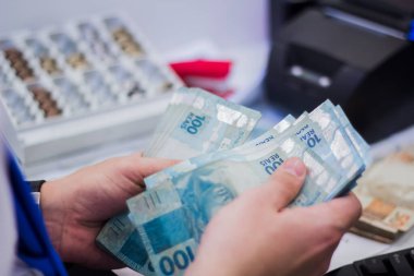 Değişim bürosu / bankada çalışan iş adamının insan eli. O para sayıyor ve bir müşteriye nakit para veriyor. Brezilya Reais 100 reais.