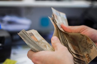 Değişim bürosu / bankada çalışan iş adamının insan eli. O para sayıyor ve bir müşteriye nakit para veriyor. Brezilyalı 50 reais fatura.